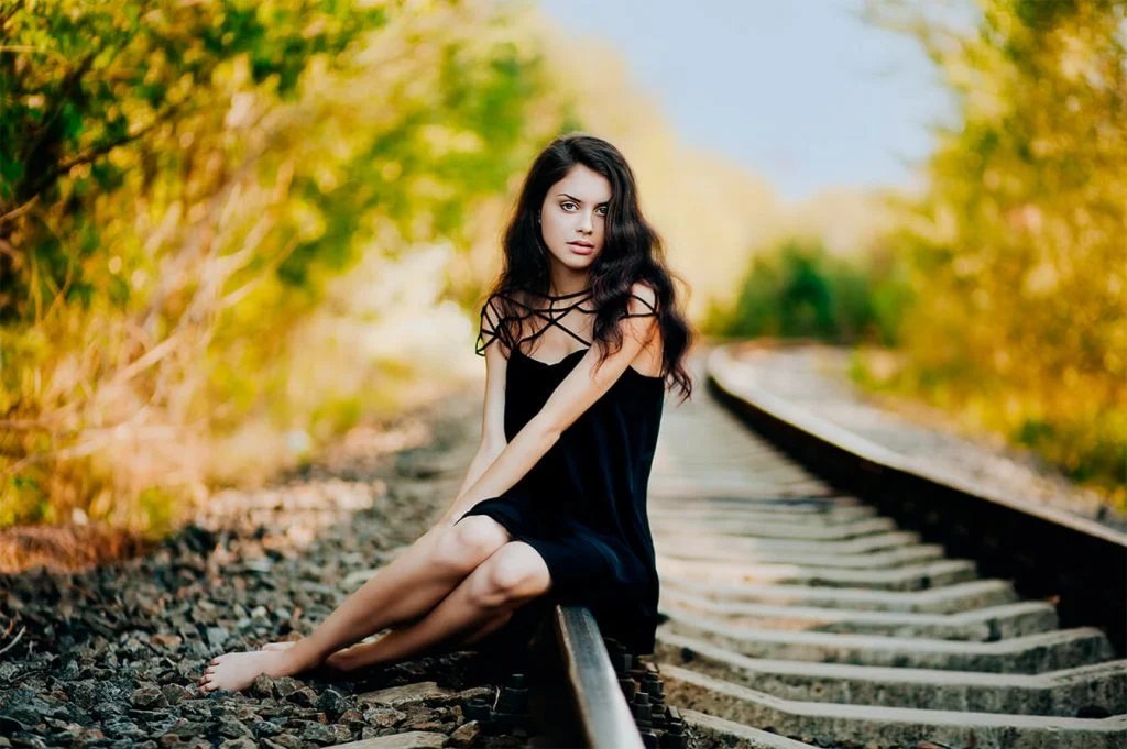 Fashion portrait of a woman sitting on railway tracks